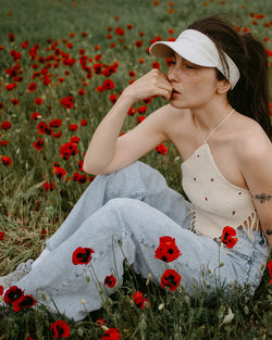 Attractive young woman sitting in the poppy field with flowers
