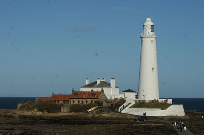 Lighthouse amidst sea and buildings against sky