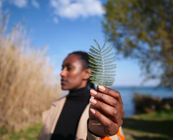 Woman holding fern against sky