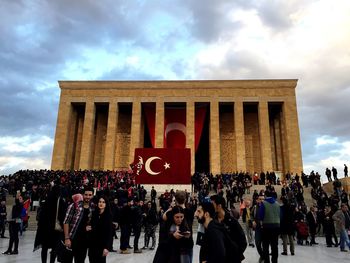 Group of people in front of building against cloudy sky