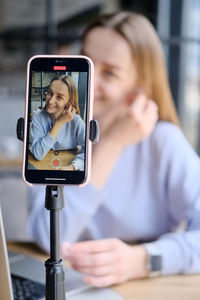 Young beautiful woman blogger making a video for her blog using phone camera in a cafe.