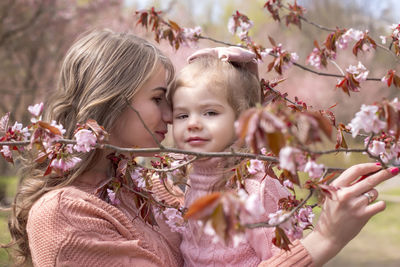 Beautiful mother hugging of little daughter in the park with blooming pink sakura.