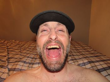 Portrait of cheerful mature man sitting against bed at home