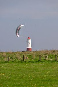 Lighthouse on field by building against sky