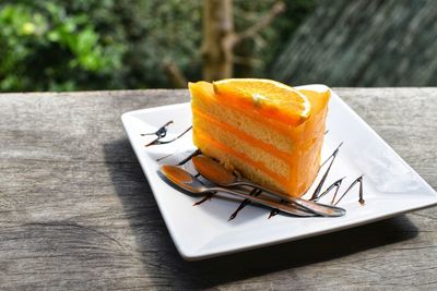 Orange cake and two spoon arrange on white disk on old wood table with nature blur background