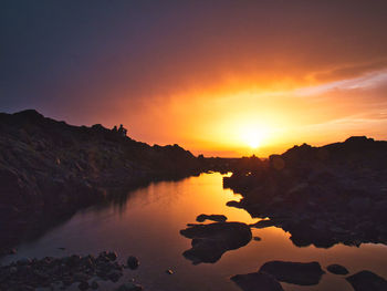 Silhouette rocks by sea against romantic sky at sunset