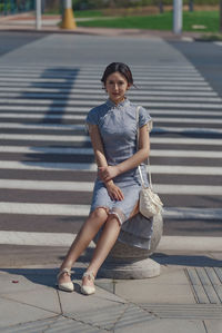 Portrait of young woman sitting on footpath