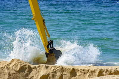 Backhoe removing sand from the beach and playing in the sea water that ends up splashing