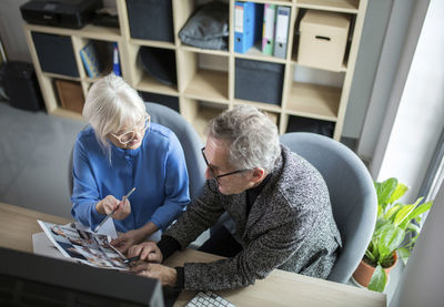 Two senior colleagues working together at desk in office discussing photos