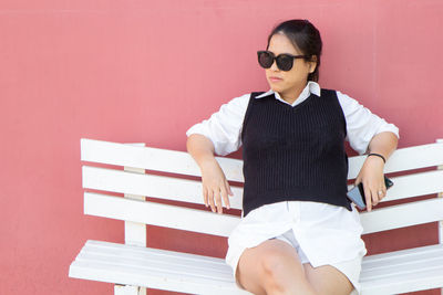 Full length of  pregnant women sitting on bench against wall