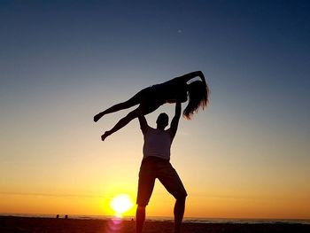 Silhouette woman on beach against clear sky during sunset