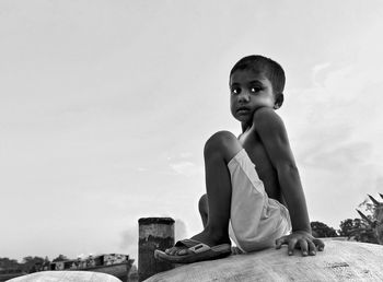 Boy looking away sitting against sky