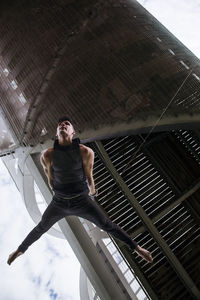 Low angle of fit male gymnast hanging on aerial straps during training in park