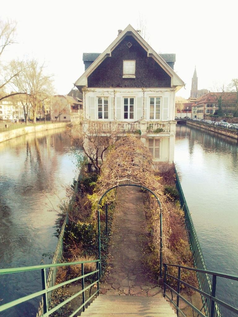 architecture, built structure, building exterior, water, the way forward, clear sky, railing, canal, diminishing perspective, river, house, walkway, tree, sky, day, footbridge, residential structure, connection, outdoors, leading