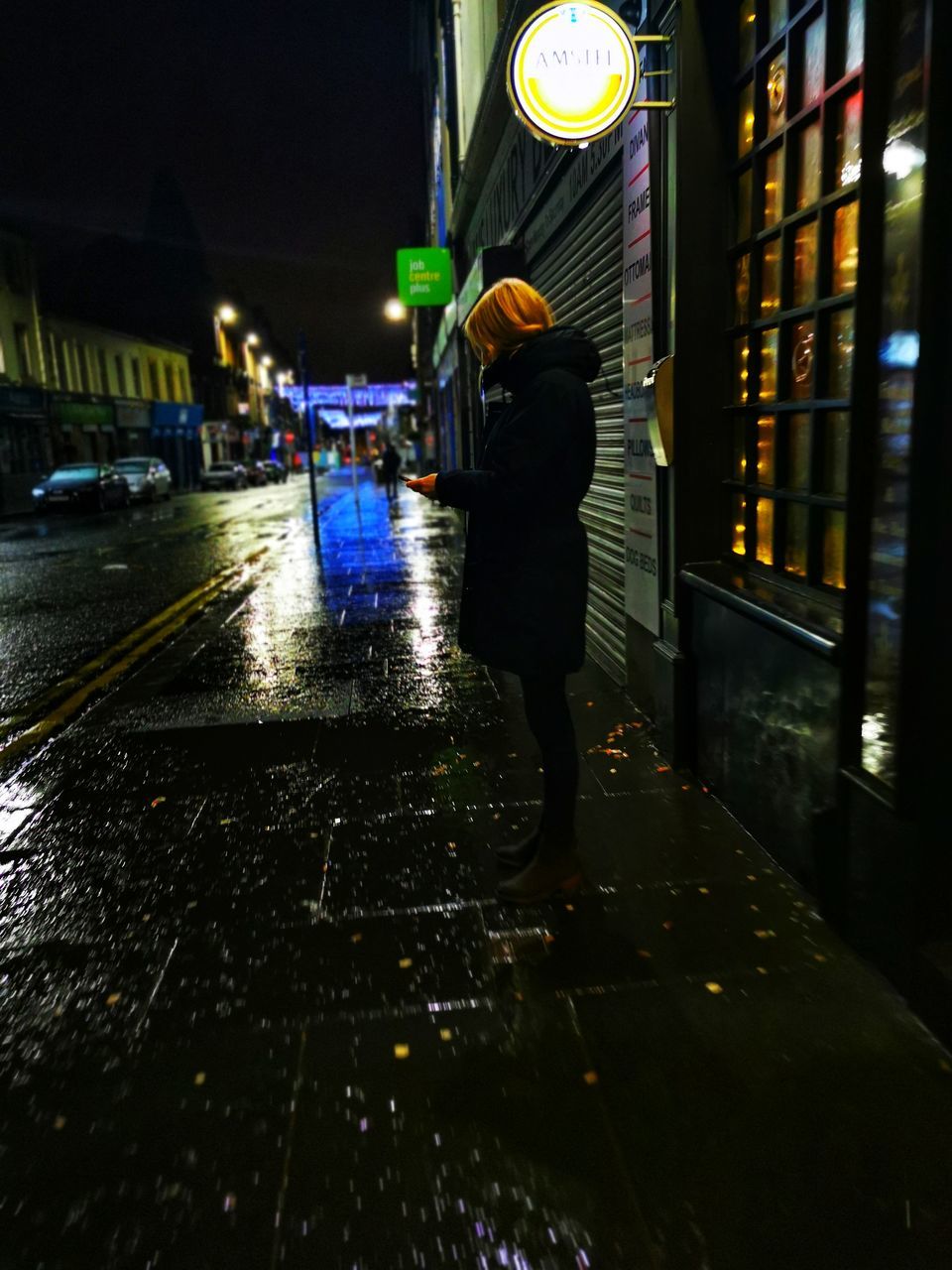 WOMAN WALKING ON WET STREET IN ILLUMINATED CITY