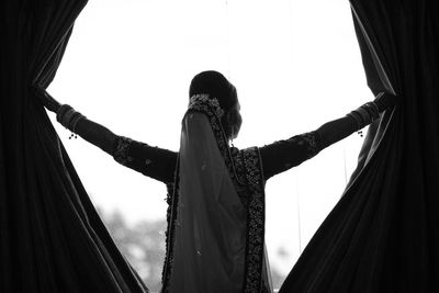 Low angle view of woman looking through curtain