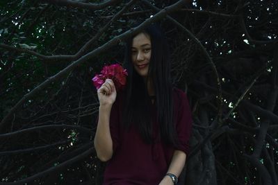 Portrait of woman holding pink flowers standing against tree