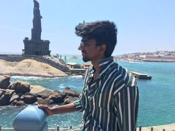 Young man looking away while standing against statue