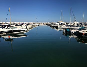 Sailboats moored at harbor against clear blue sky