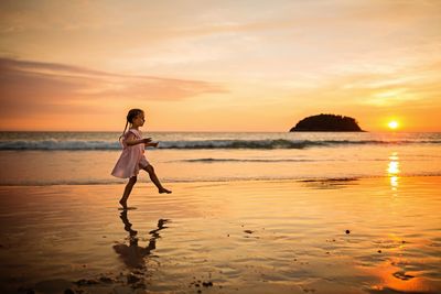 Full length of girl walking at beach against sky during sunset