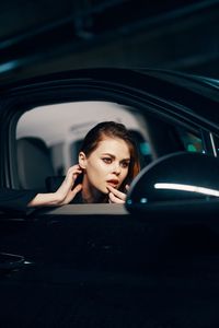 Young woman looking in side-view mirror of car