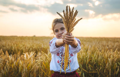 Portrait of girl holding wheat standing at farm