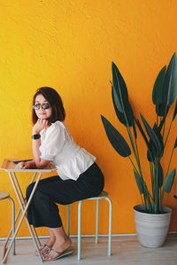 Young woman sitting on table against wall