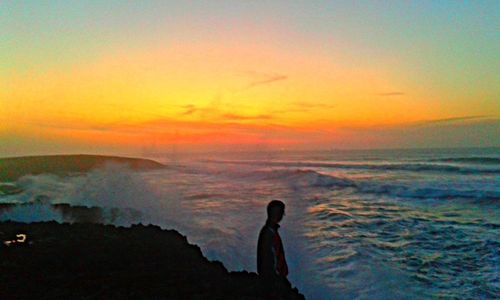 Silhouette of man standing on rock in sea