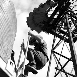 Low angle view of man moving up on ladder against sky