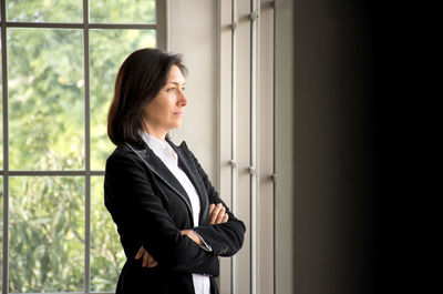 Smiling businesswoman looking through window while standing at office