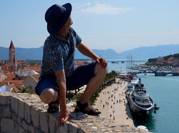 Rear view of woman sitting on rock by sea against sky