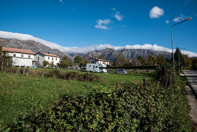 Plants growing on field by houses against sky