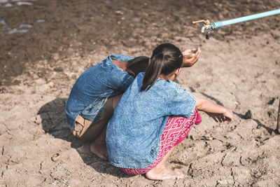 Siblings crouching by tap on drought field