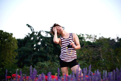 Men with closed eyes holding digital camera standing admist plants against sky