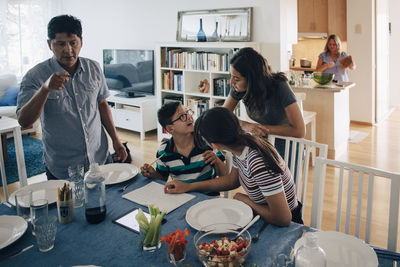 Sisters looking at boy while father standing by dining table