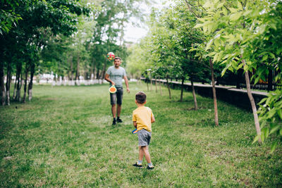 Full length of father and son playing on grass against trees