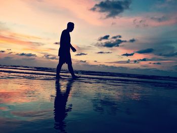 Silhouette man standing on beach against sky during sunset