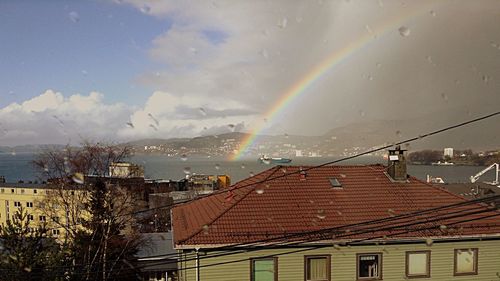 Rainbow over city against cloudy sky