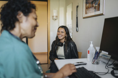 Happy young woman sitting by female doctor at desk in clinic