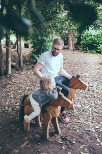 High angle view of father and daughter sitting on wooden horses at park