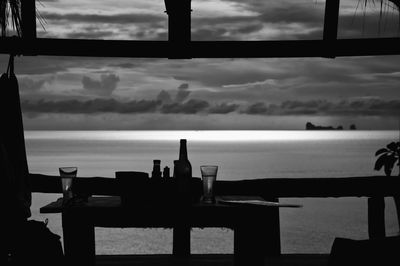 Empty chair by sea against sky seen through window