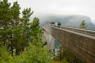 People on footbridge by mountains against sky