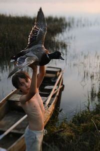 Boy holding bird while standing by boat on lake