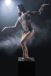 Young woman dancing on box against black background