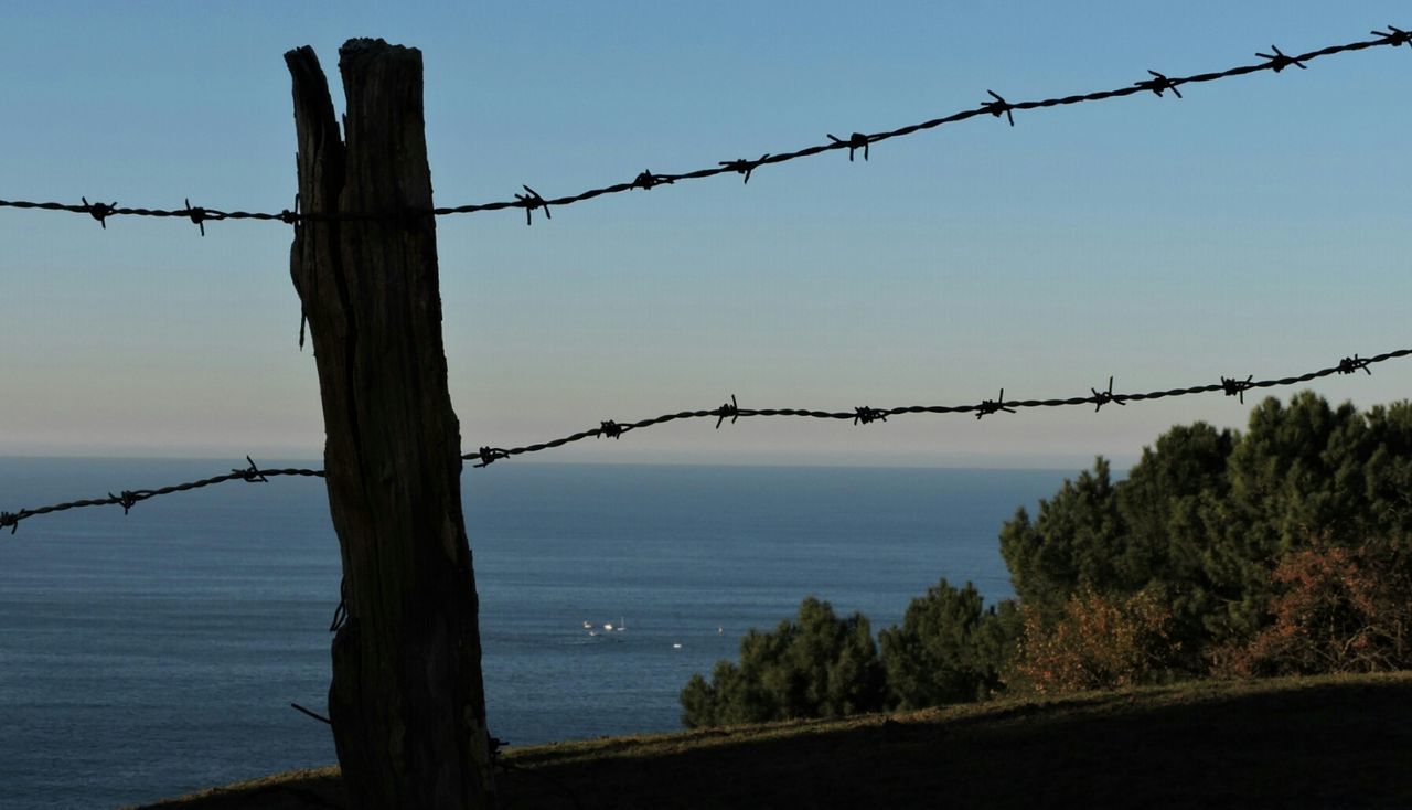 water, sea, barbed wire, fence, safety, protection, security, sky, clear sky, tranquility, silhouette, horizon over water, nature, tranquil scene, connection, bird, metal, outdoors, no people, scenics