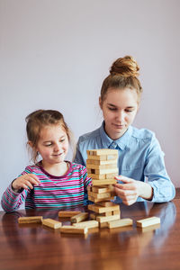 Cheerful girls playing with block sitting on table