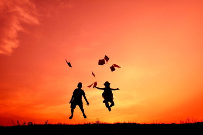 Silhouette  of two children throwing papers against sky at sunset