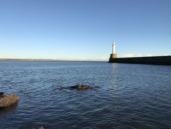 Lighthouse by sea against clear sky