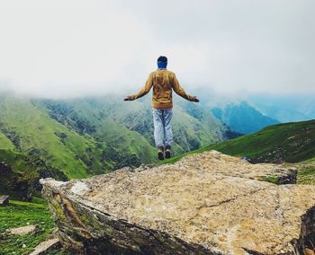 Rear view of man levitating on mountain against sky