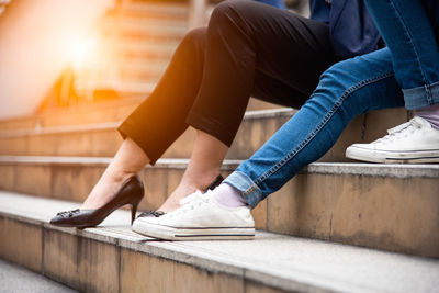 Low section of couple sitting on steps during sunny day